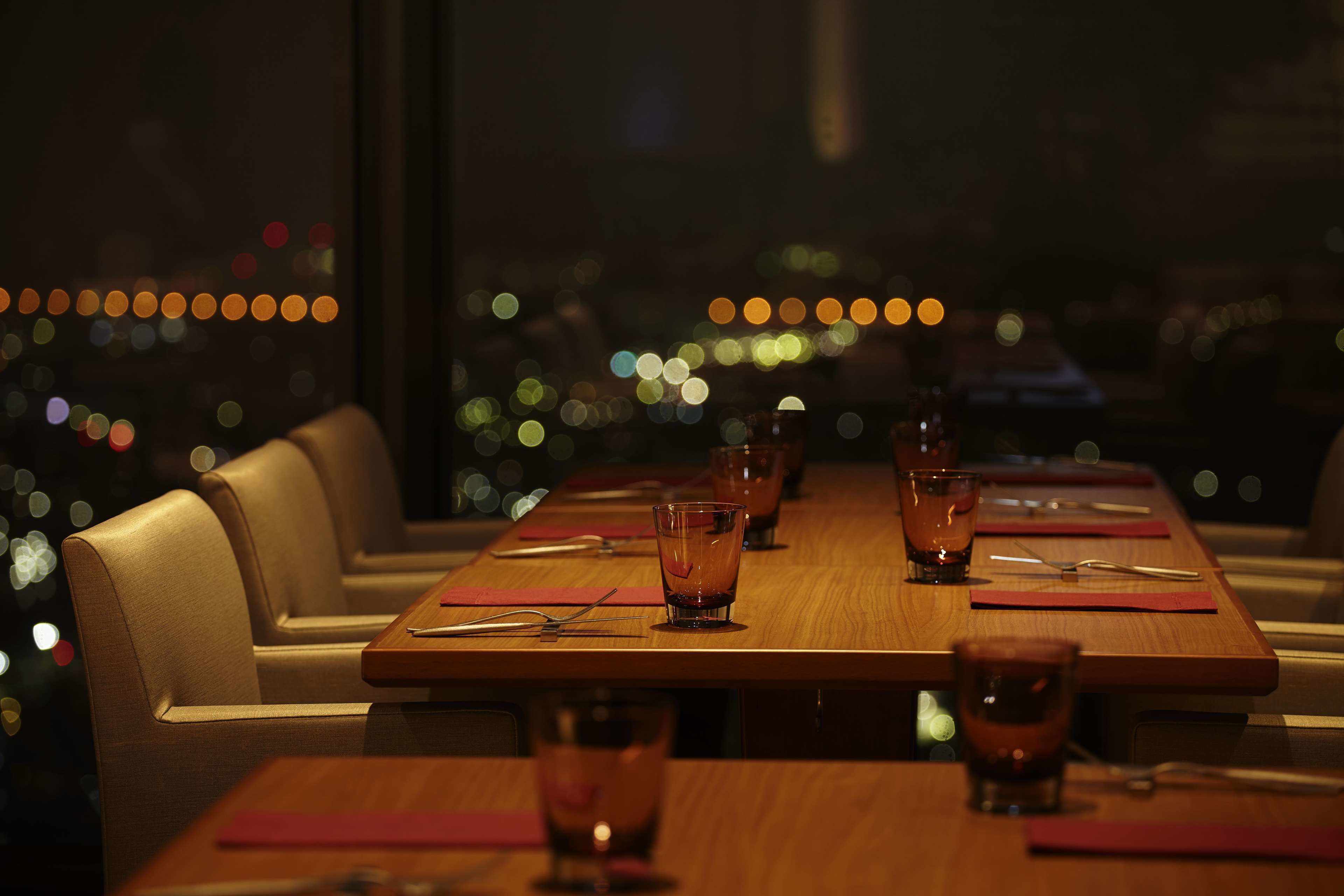 Un restaurante con una larga mesa de madera dispuesta para comer, con vasos y cubiertos sobre la mesa.