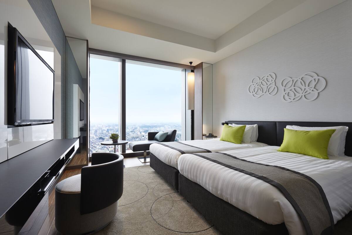 A modern hotel room with a large bed, a desk, and a view of the city.