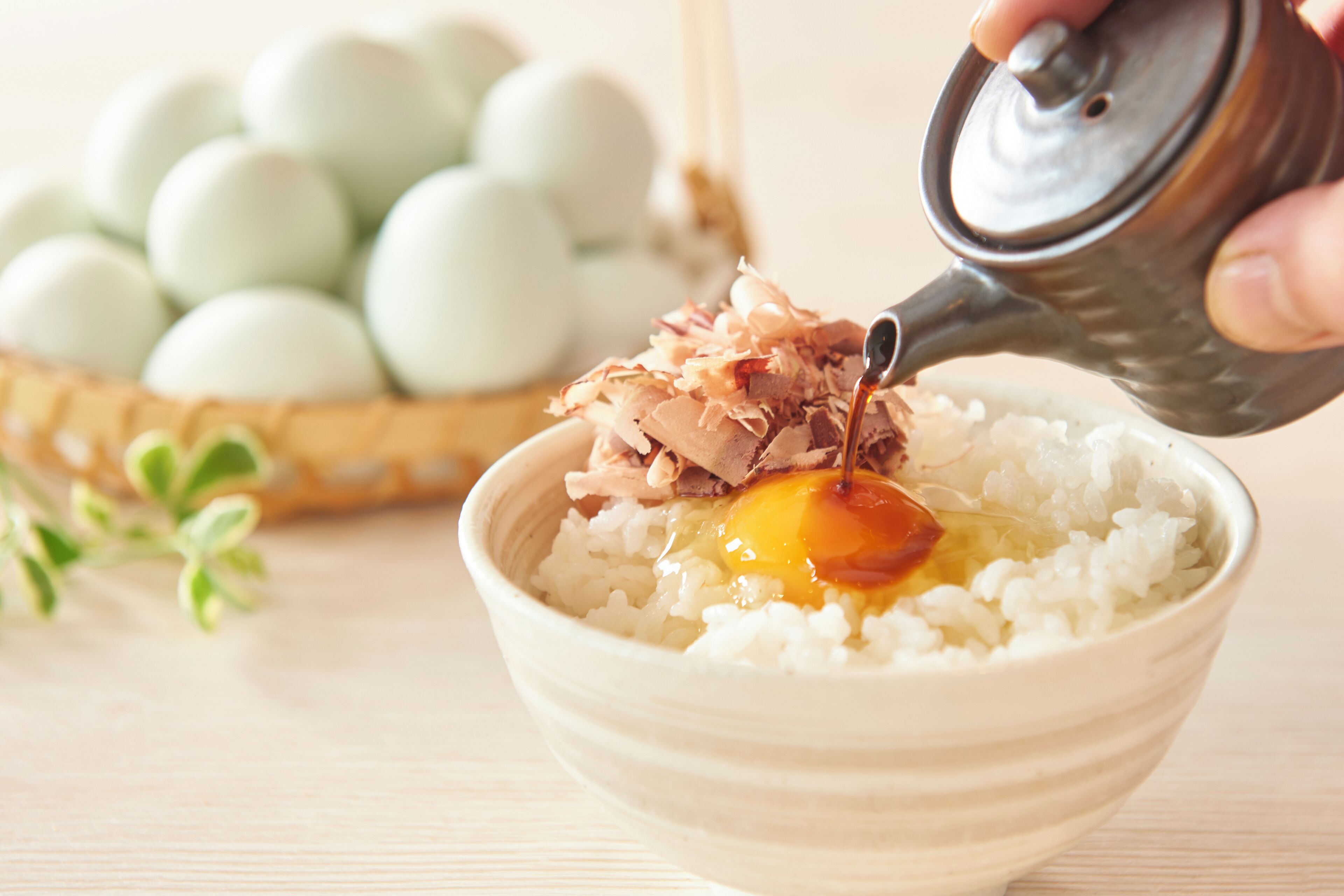 A bowl of rice with a raw egg and shredded meat, with a teapot pouring a liquid over it.