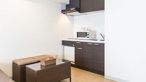 A compact kitchenette with dark wooden cabinets, a microwave, and a glass-top table with a cushion. - Condominium Hotel Monpa (Chatan)