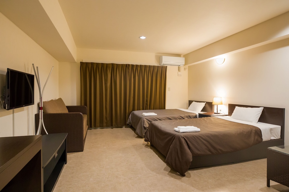 A hotel room with two beds, a TV, a desk, and a window with curtains.