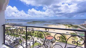 Un balcón con vistas a una playa y al océano, con barandilla metálica y detalles ornamentales.