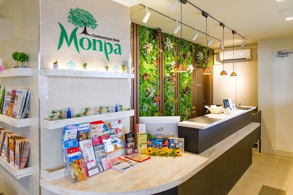 A hotel reception area with a modern design, featuring a reception desk, a wall-mounted plant display, and various informational brochures. - Condominium Hotel Monpa (Chatan)