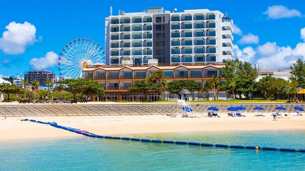 A beachfront hotel with a Ferris wheel in the background, a pool area, and beach chairs. - Condominium Hotel Monpa (Chatan)