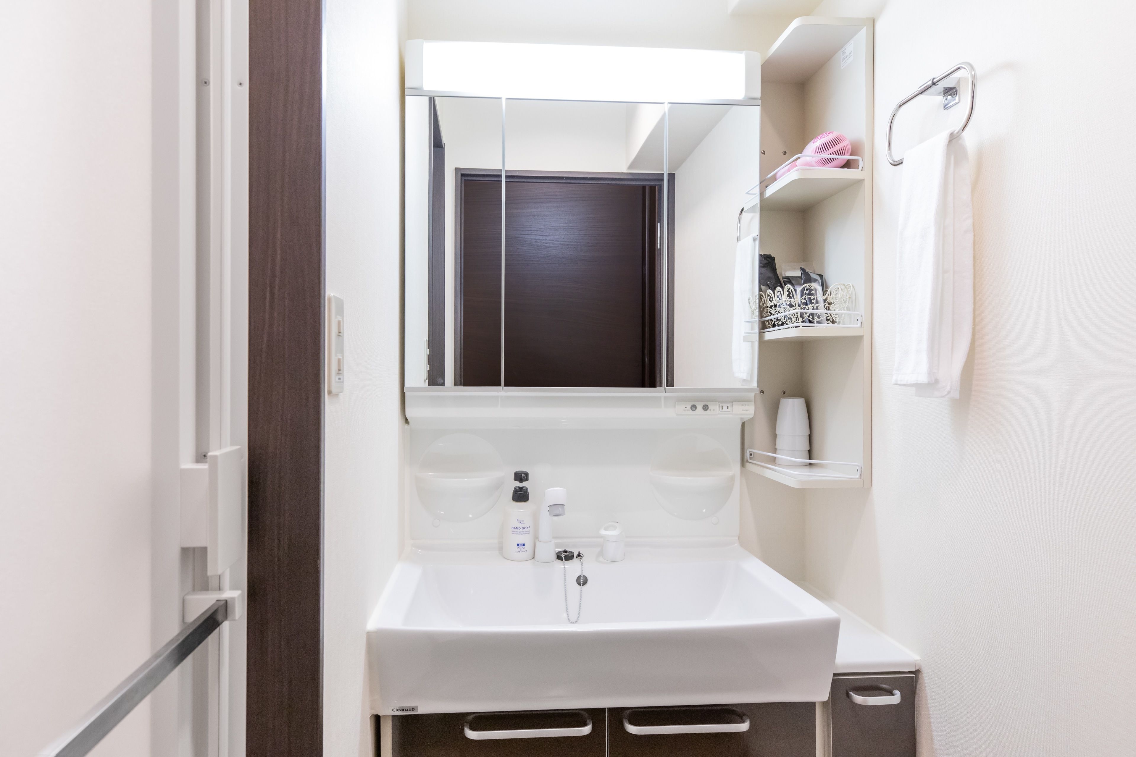 Un bany petit i funcional amb un lavabo blanc, un mirall a sobre i una tovallola penjada a un escorredor.