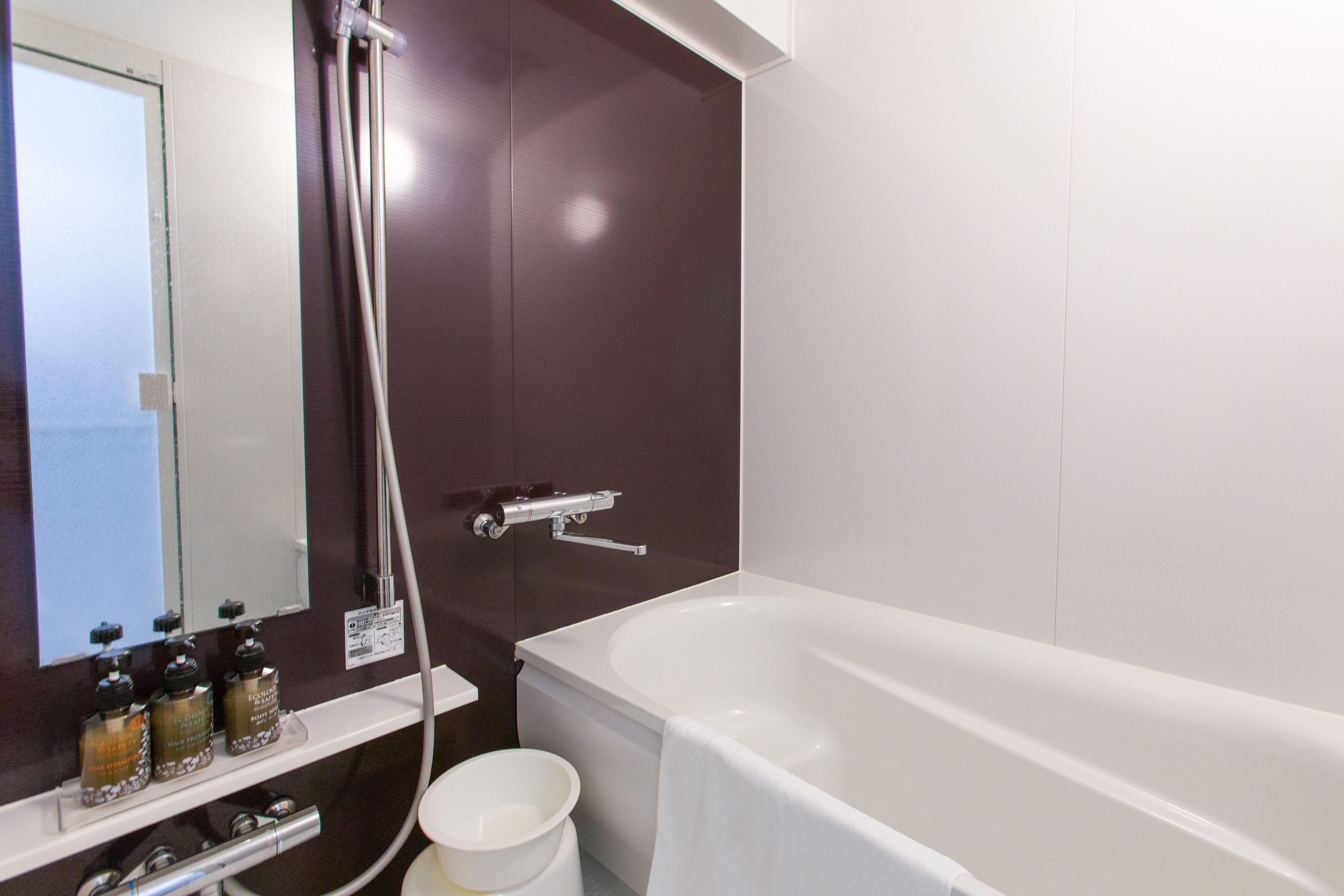 A modern bathroom with a white bathtub, a showerhead, and a mirror above a shelf with toiletries.