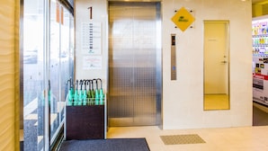 An elevator with a sign indicating the first floor, a vending machine, and a glass door with umbrellas. - Condominium Hotel Monpa (Chatan)