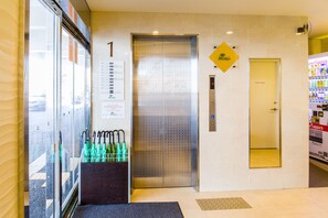 An elevator with a sign indicating the first floor, a vending machine, and a glass door with umbrellas. - Condominium Hotel Monpa (Chatan)