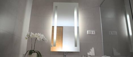 Un baño moderno con un espejo grande, un lavamanos blanco y una orquídea en maceta.
