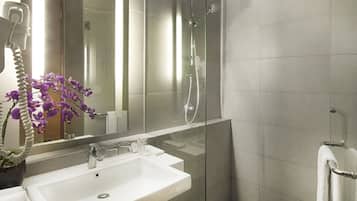 A modern bathroom with a large mirror, a white sink, a glass shower enclosure, and a potted orchid.