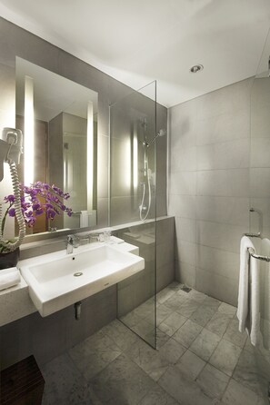 A modern bathroom with a large mirror, a white sink, a glass shower enclosure, and a potted orchid. - D'primahotel Tangerang (Tangerang)