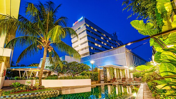 A hotel with a pool, palm trees, and a night sky. - D'primahotel Tangerang (Tangerang)