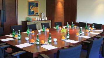 Ein Konferenzraum mit langem Tisch, gedeckt für Besprechungen, ausgestattet mit Stühlen, Wasserflaschen und Obstschalen.