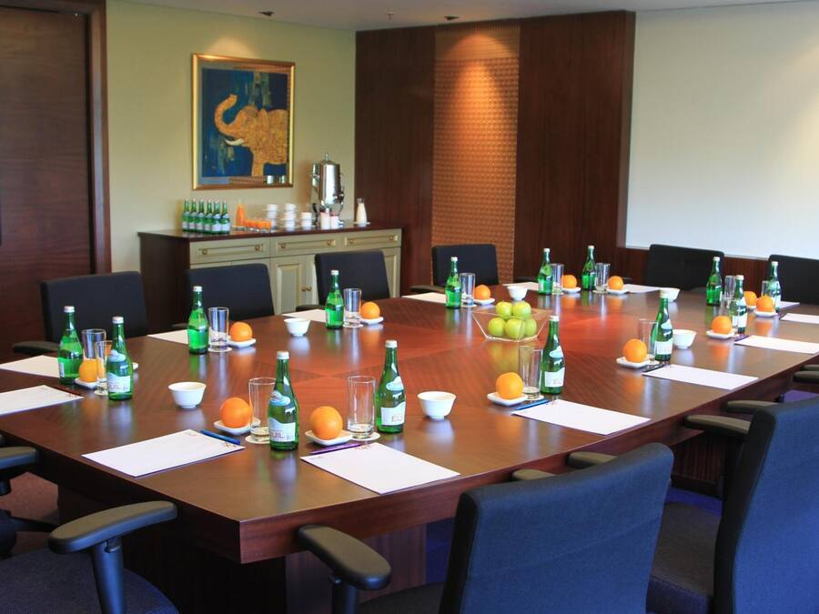 Ein Konferenzraum mit langem Tisch, gedeckt für Besprechungen, ausgestattet mit Stühlen, Wasserflaschen und Obstschalen.