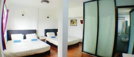 A hotel room with a large bed, a smaller bed, a desk, and a sliding glass door leading to a bathroom.