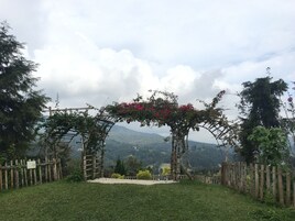 Ein Garten mit einem hölzernen Bogen, einem Holzzaun und Blick auf ferne Berge.