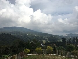 A mountainous landscape with scattered buildings, a wooden fence, and a cloudy sky.