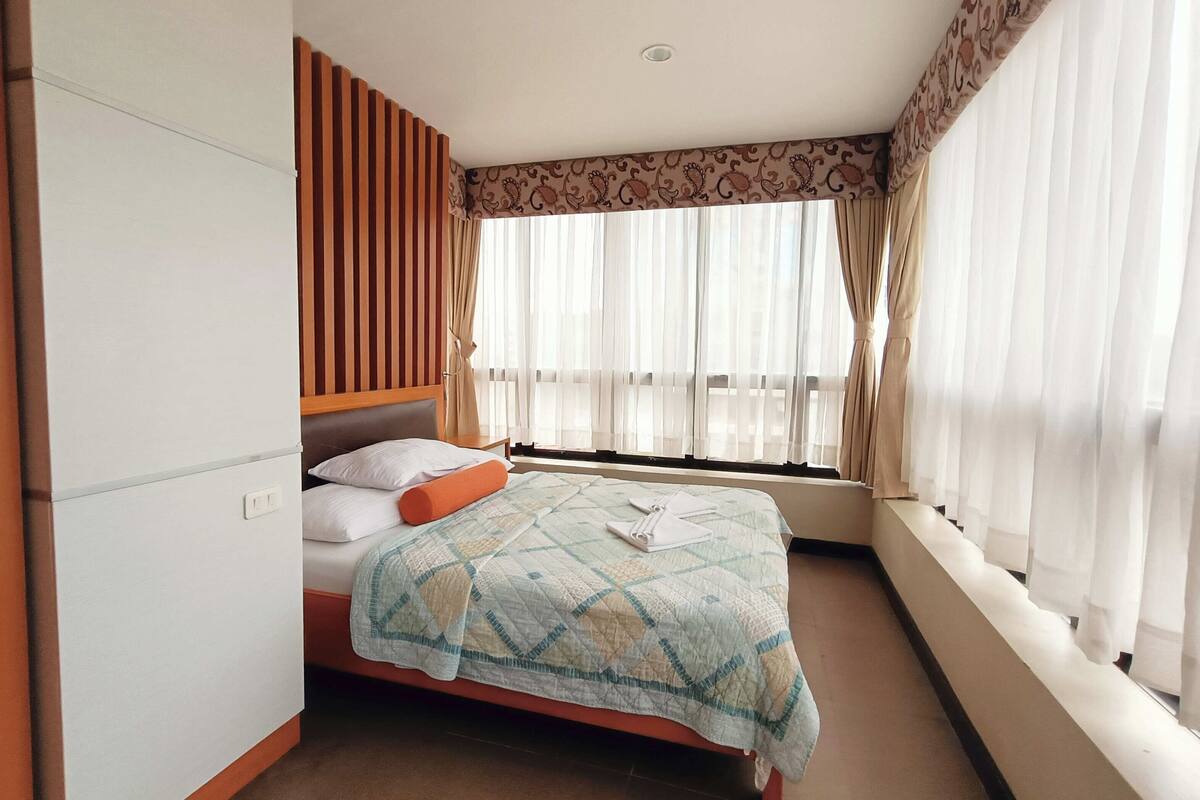 A hotel room with a bed, a wardrobe, a window with curtains, and a patterned headboard.