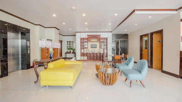 Un hall d’entrée avec un canapé jaune, deux fauteuils bleu clair, une table basse en bois et un comptoir de réception portant l’inscription « FOBS ».