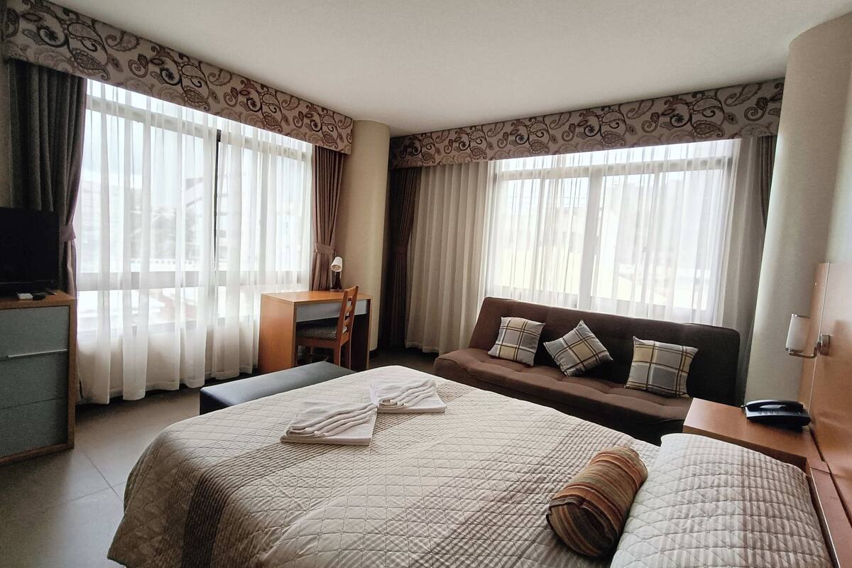 A hotel room with a large bed, a sofa, a desk, and a television.
