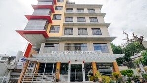 Un hôtel à plusieurs étages au design moderne, doté d’une entrée imposante avec une façade en verre et d’une enseigne indiquant « Fuente Oro Business Suites ».