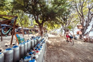 A beachside area with a row of metal tanks, a sign with a cartoon character, and a person riding a bicycle.