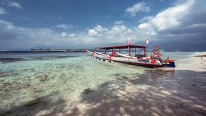Un bote con diseño rojo y blanco amarrado en una playa de arena y aguas cristalinas.