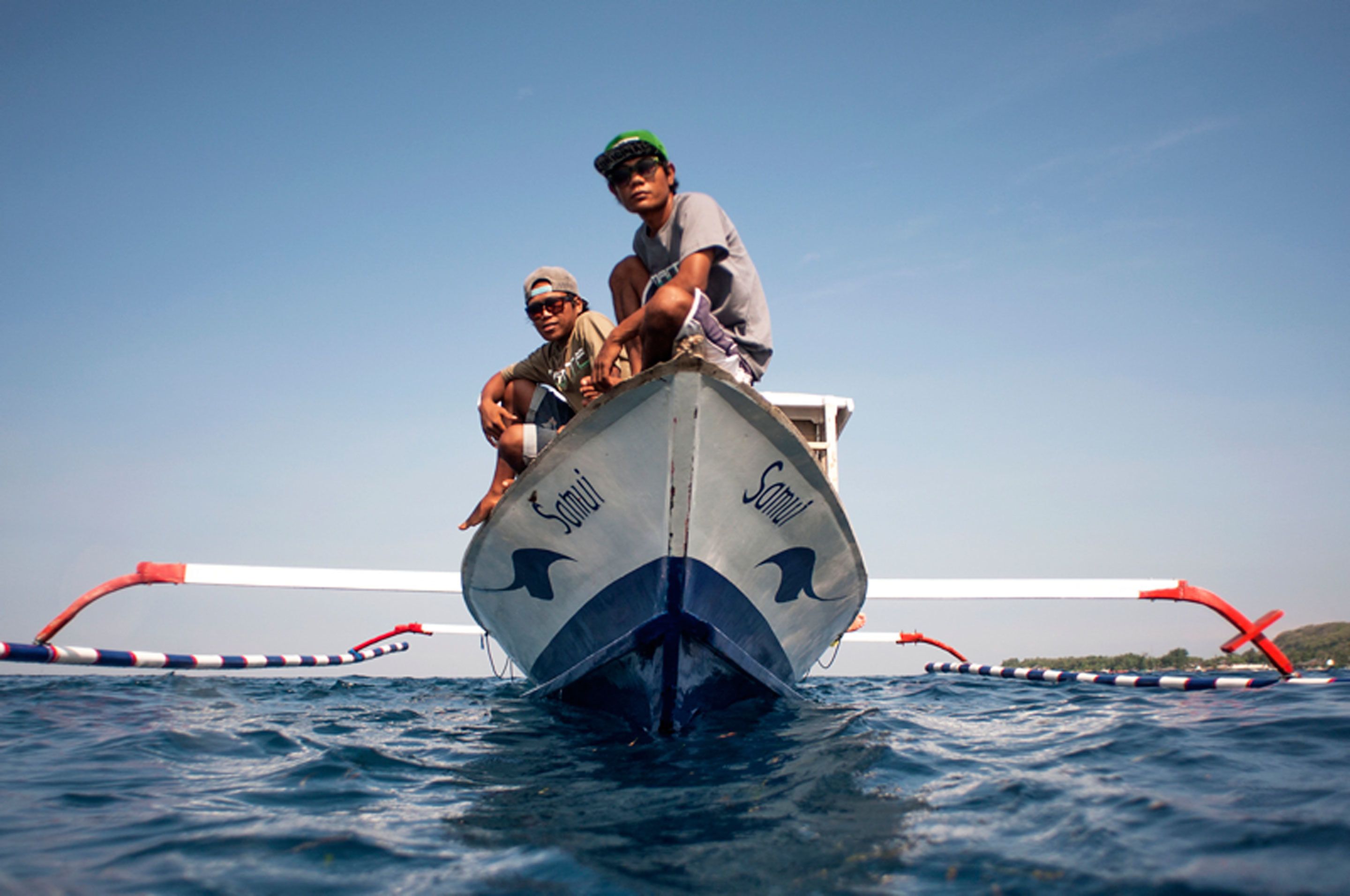 A boat with two people on the bow, a clear sky, and calm water.
