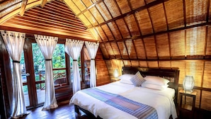 Un dormitorio amplio con una cama grande, techo de madera y vistas al verdor exterior.