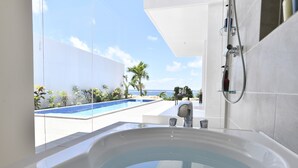 Un baño moderno con una bañera grande, una ducha y vistas a una piscina y palmeras.