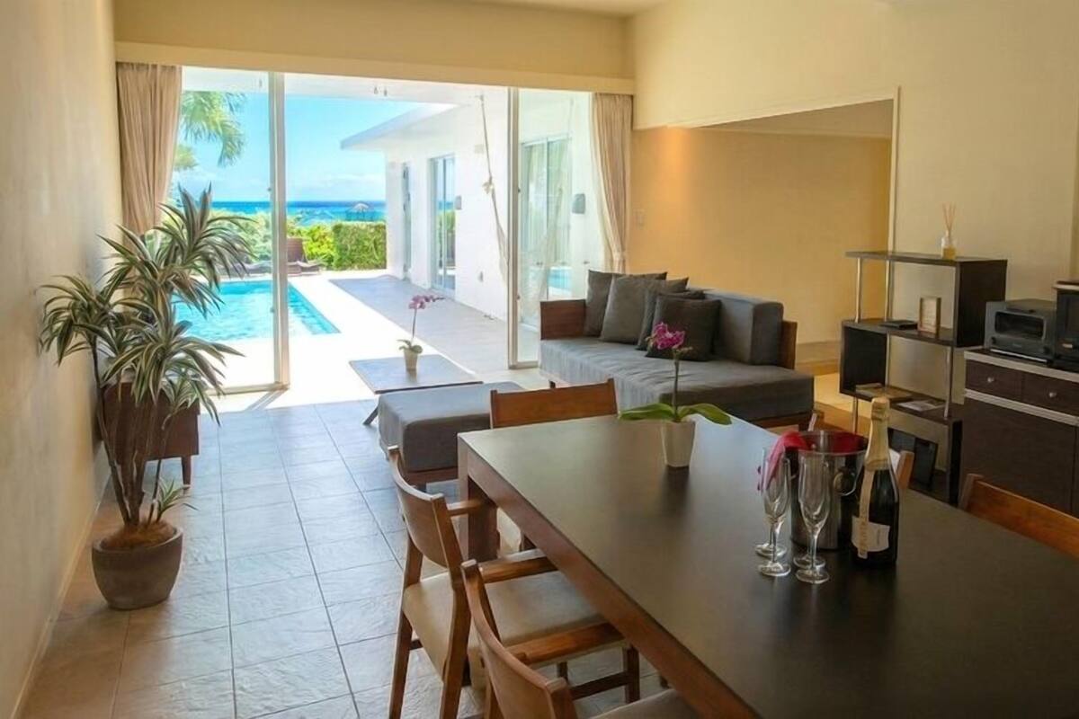 A modern hotel room with a dining area, a sofa, a TV, and a view of the ocean.