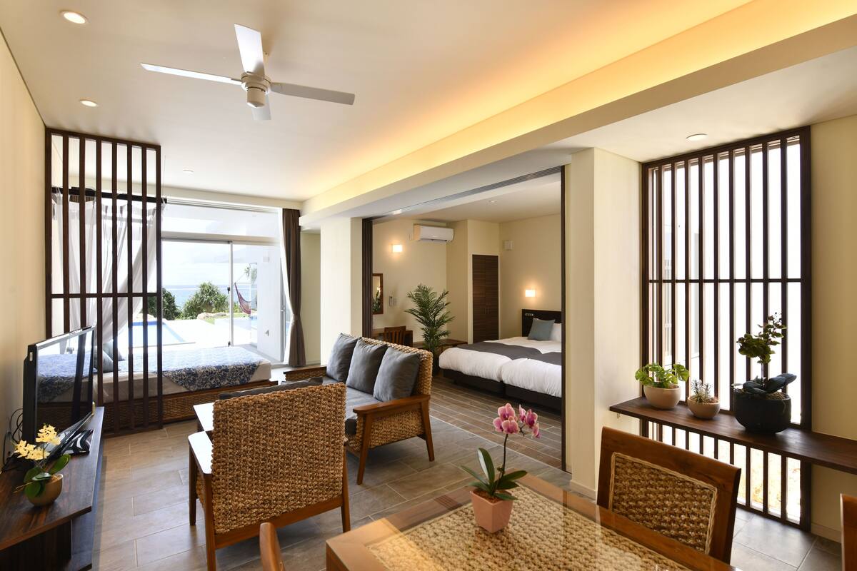 A modern hotel room with a balcony, a sofa, a dining table, and a bed.