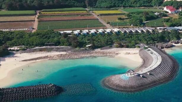 Una zona costera con una playa, una estructura circular de piedra y una hilera de edificios.