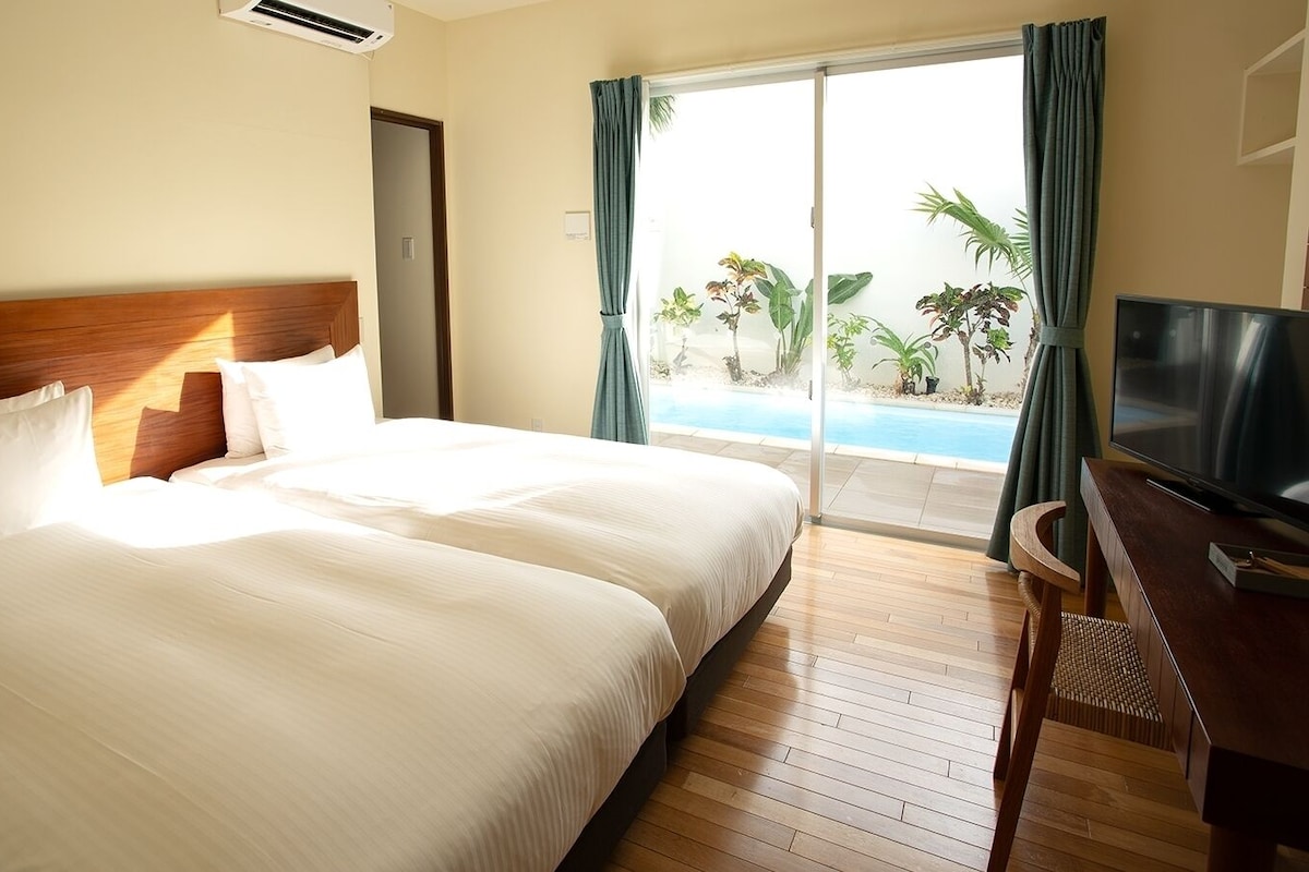 Habitación de hotel con una cama grande, televisión, escritorio y vista a una piscina.