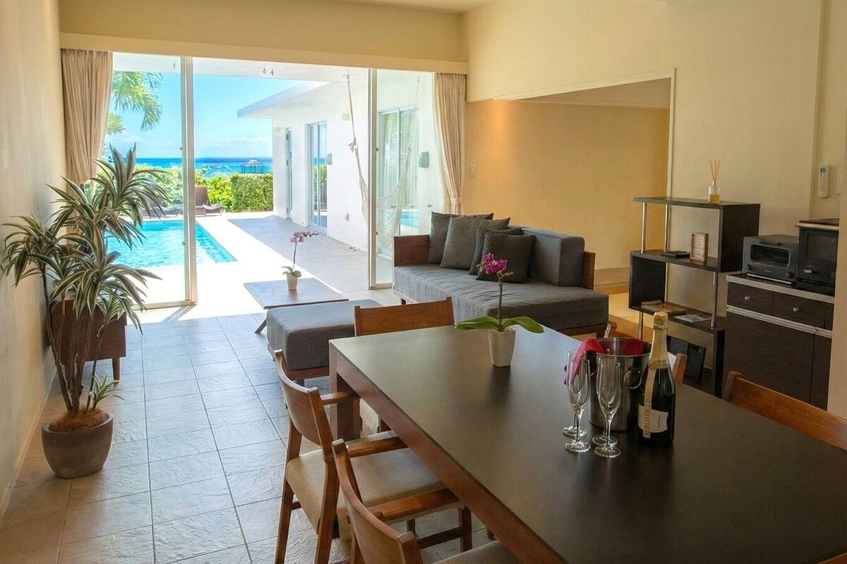 A modern kitchen with a dining area, a sofa, and a view of the pool and ocean.