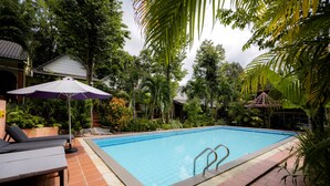 A swimming pool with tiled edges, surrounded by lush greenery and a tiled patio area with lounge chairs and an umbrella. - Mai Phuong Binh Bungalow (Phu Quoc)
