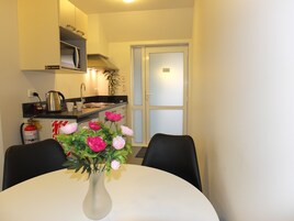 Cocina pequeña y moderna con microondas, hervidor y lavabo. Hay una mesa de comedor con sillas y un jarrón de flores.