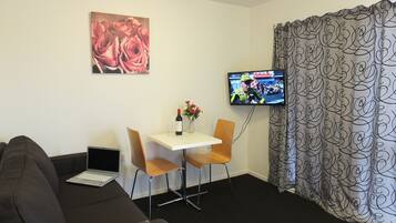 Une chambre d’hôtel avec un canapé, une petite table surmontée d’un vase de fleurs, un téléviseur fixé au mur et des rideaux à motifs.