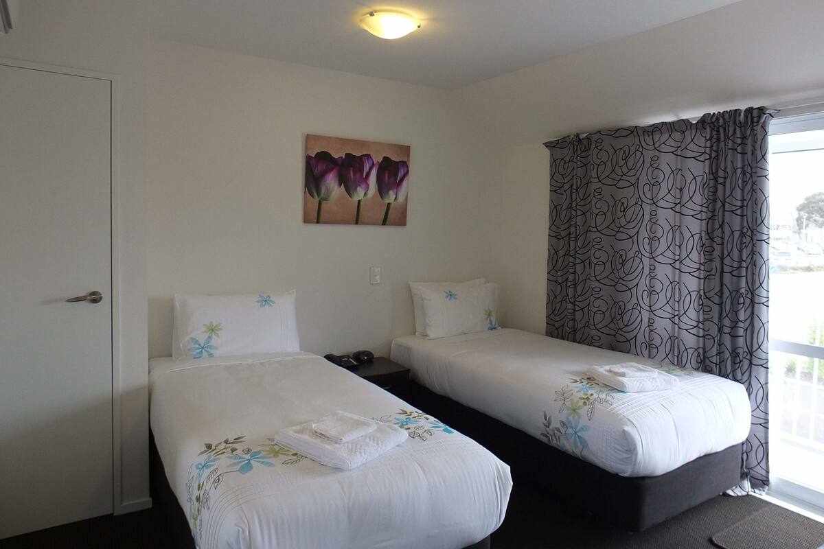 A hotel room with two beds, a painting of tulips, a patterned curtain, and a door.