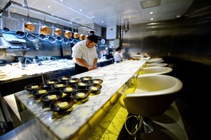 Une cuisine dotée d’un plan de travail en marbre, de plusieurs casseroles suspendues au-dessus, et d’une rangée d’éviers.