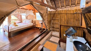 A tent-style room with a bed, a small table, a chair, and a shelf with a lamp. - La Cocoteraie Ecolodge- Glamping (Gili Trawangan)