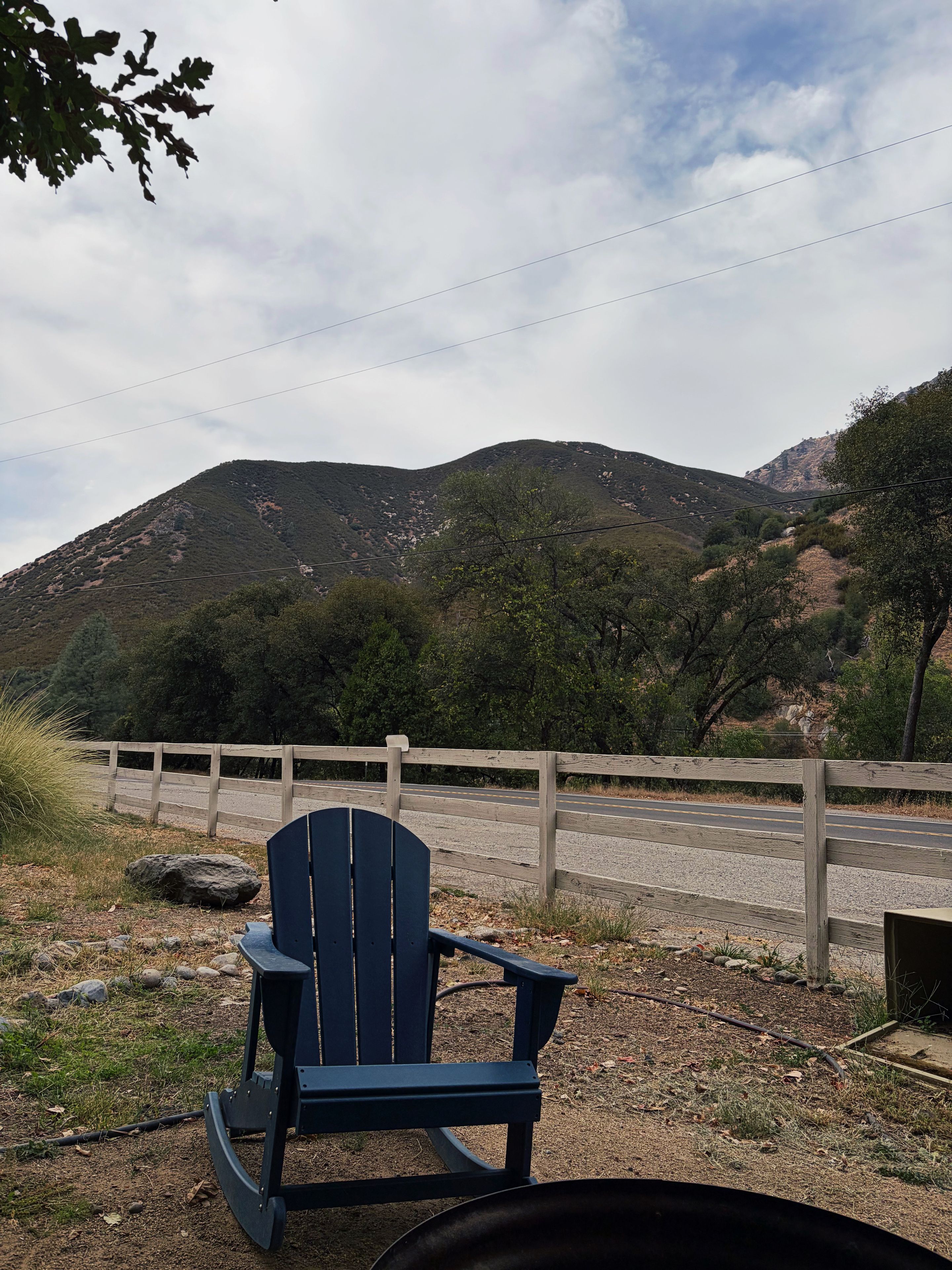 Une chaise Adirondack bleue, placée dans un cadre naturel, avec vue sur une montagne et une clôture en bois.