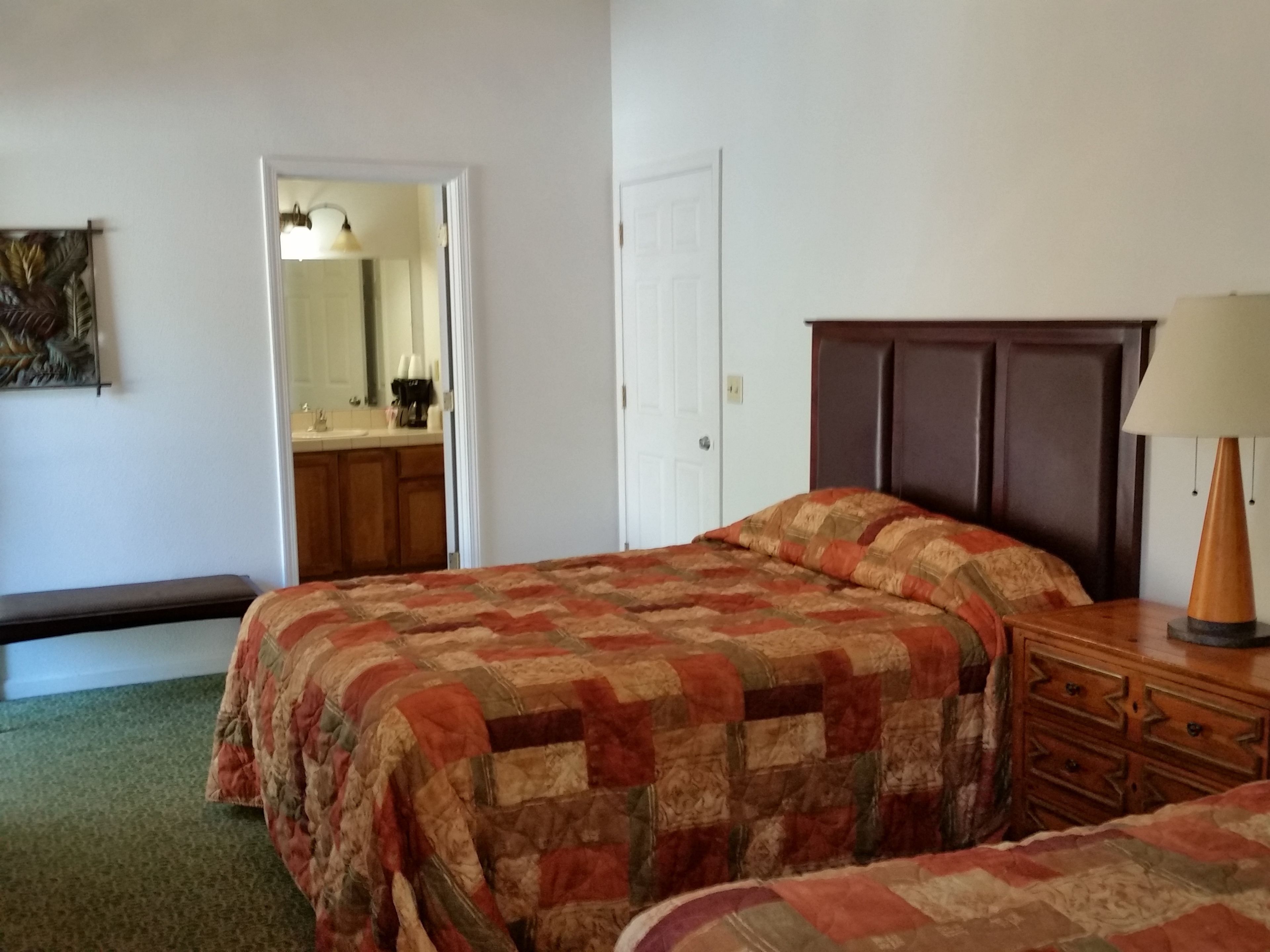 A bedroom with a bed, a dresser, a mirror, and a door leading to a bathroom.