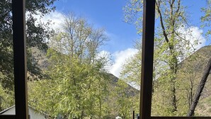 A wooden deck with a pathway leading to a white building surrounded by trees and a mountain in the background. - Indian Flat RV Park - Tent Cabins & Cottages (El Portal)