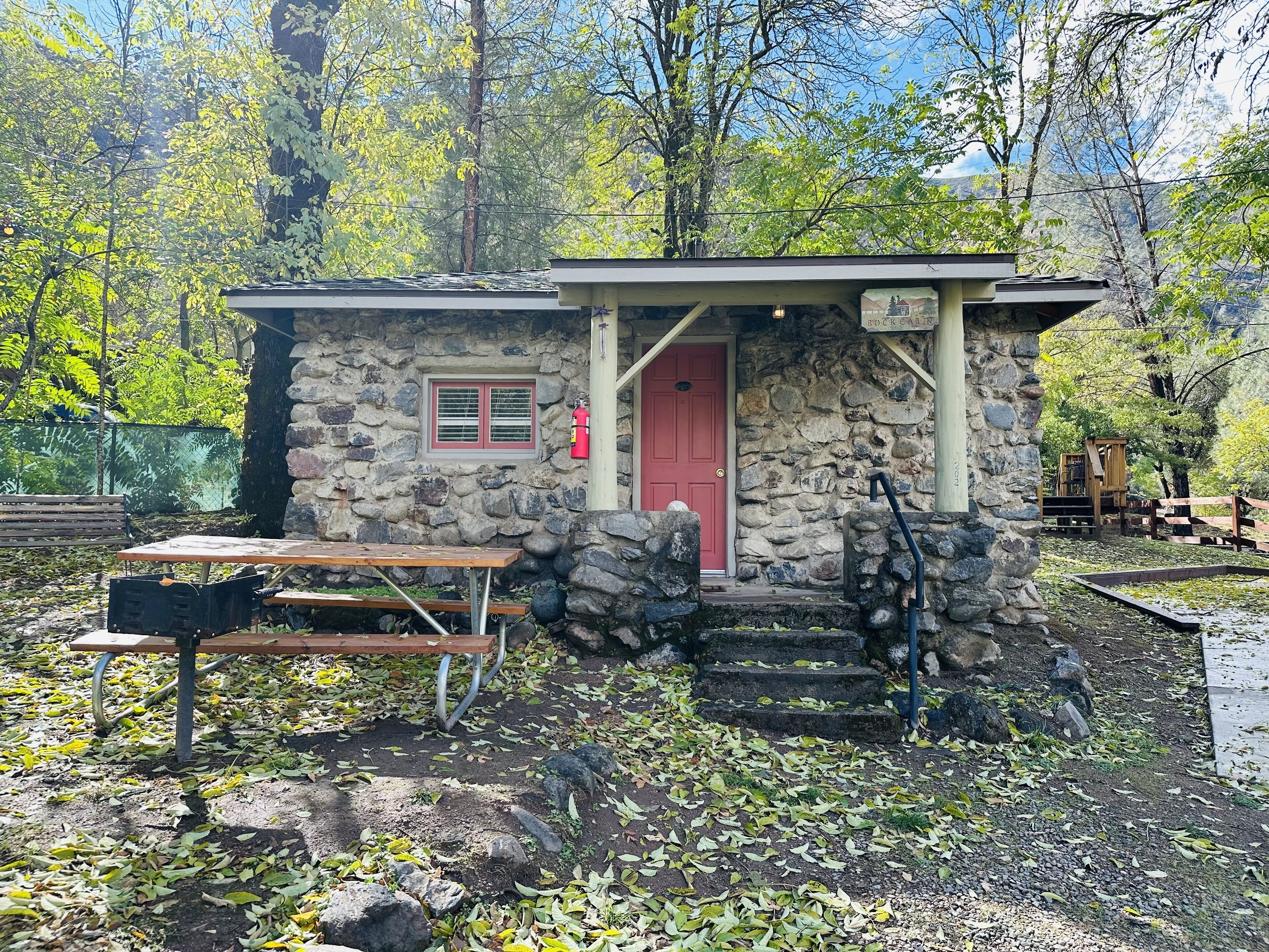 A rustic stone cabin with a red door, a small window, and a wooden bench outside.