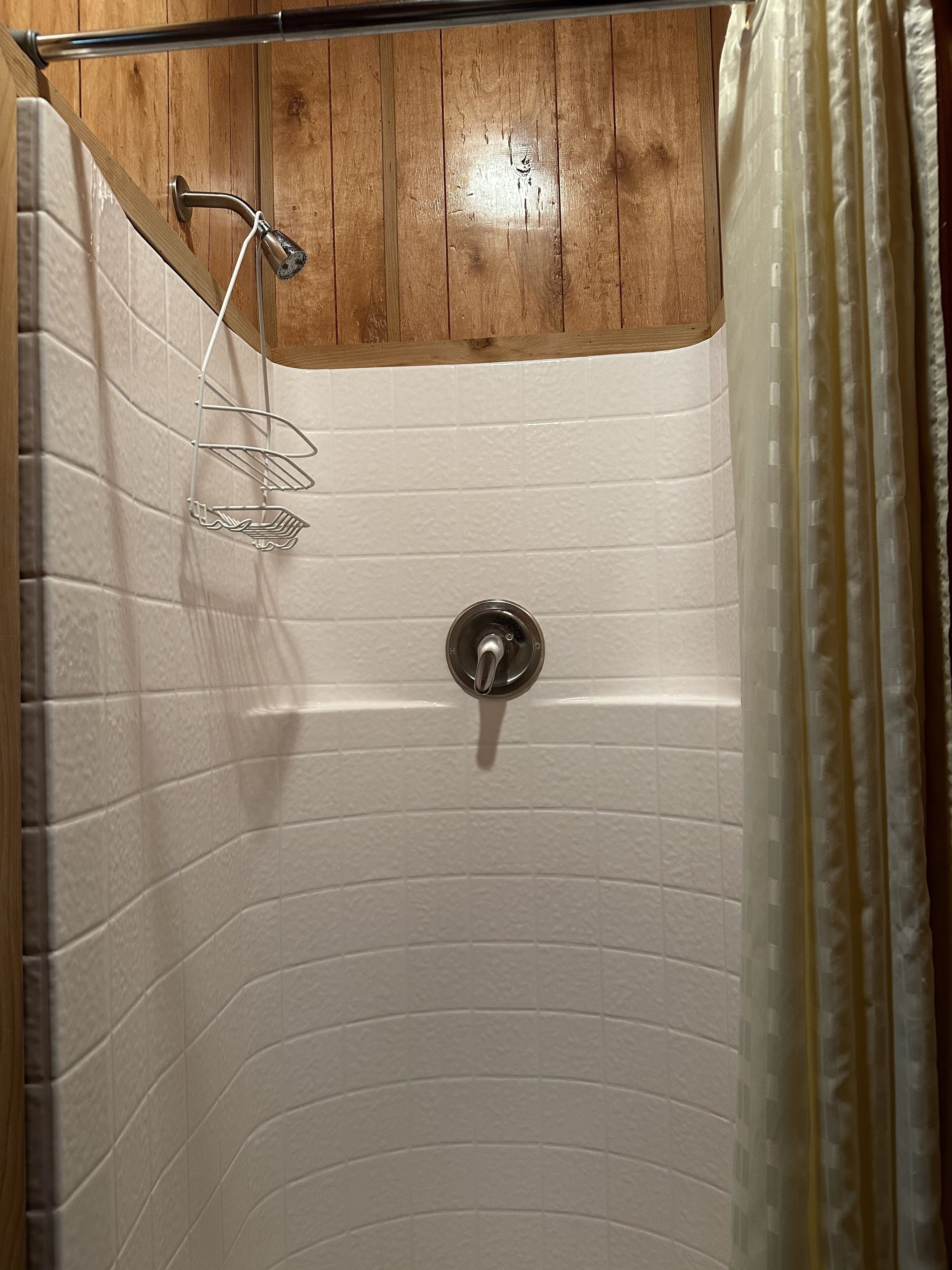 A shower with a wooden ceiling, white tiled walls, and a metal showerhead.