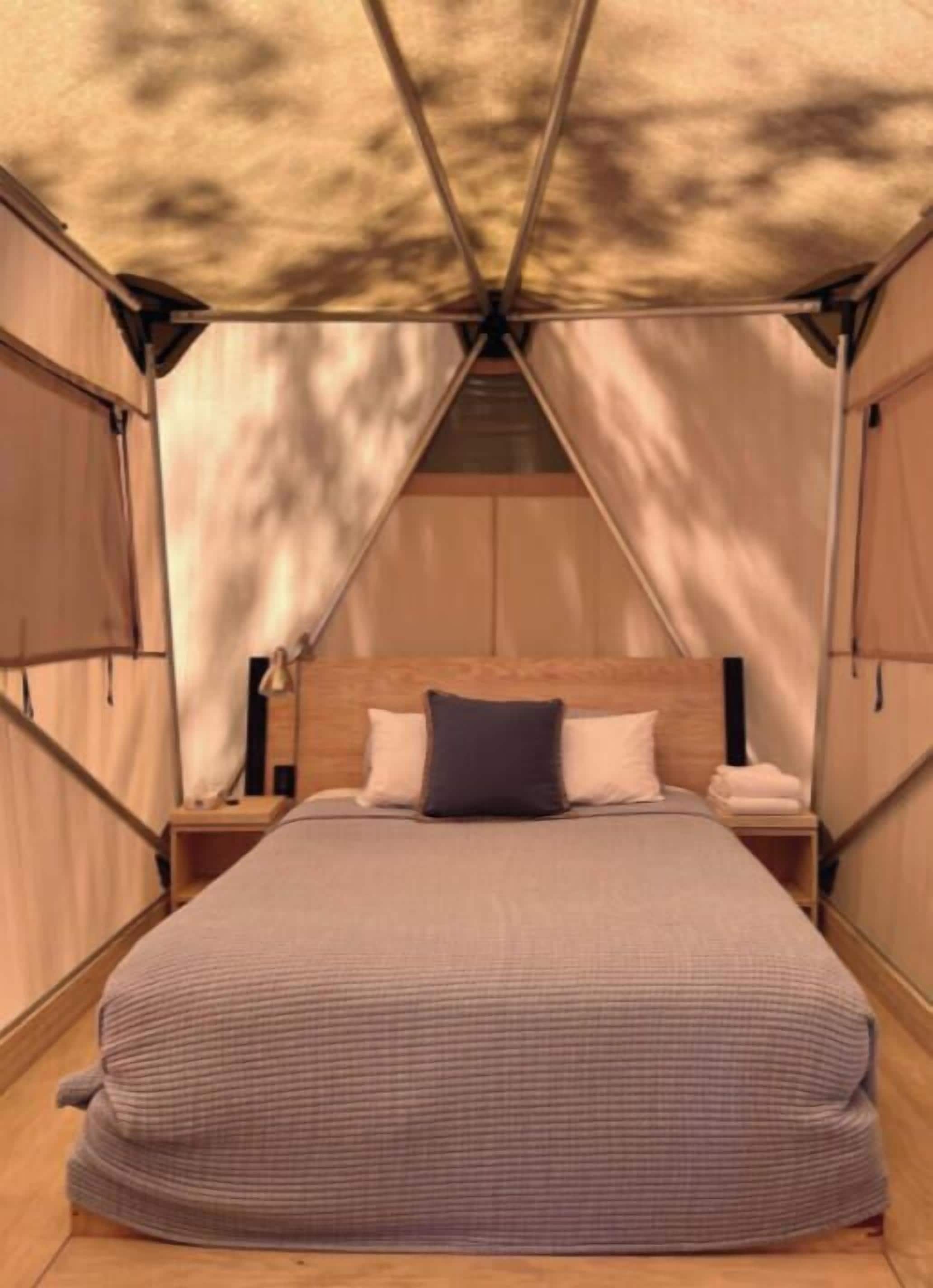 Een tent met een bed, kussens en een nachtkastje.