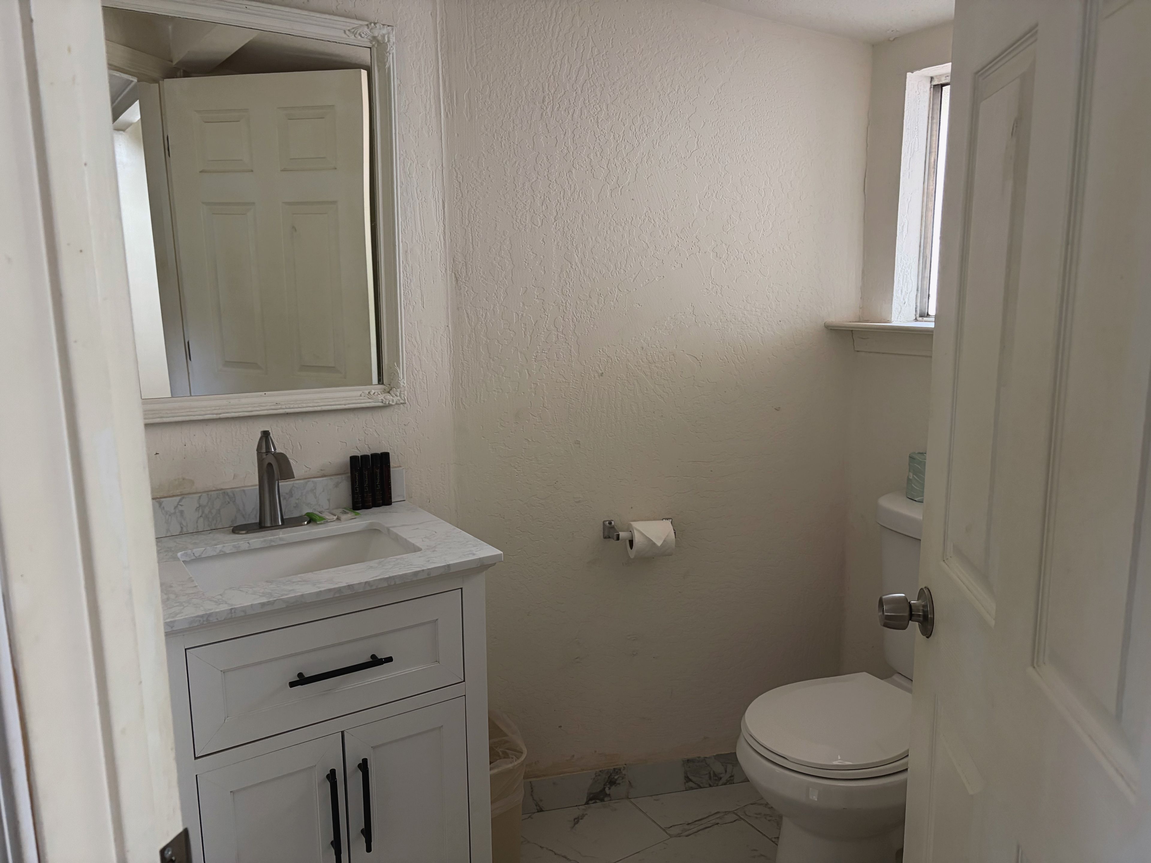 A compact bathroom with a white sink, a mirror, a toilet, and a door.