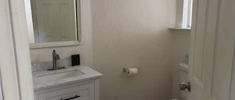 A compact bathroom with a white sink, a mirror, a toilet, and a door.
