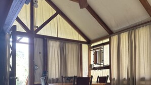 A room with a wooden ceiling, a bed with a patterned blanket, a dining table with chairs, and a view of the outdoors. - Indian Flat RV Park - Tent Cabins & Cottages (El Portal)